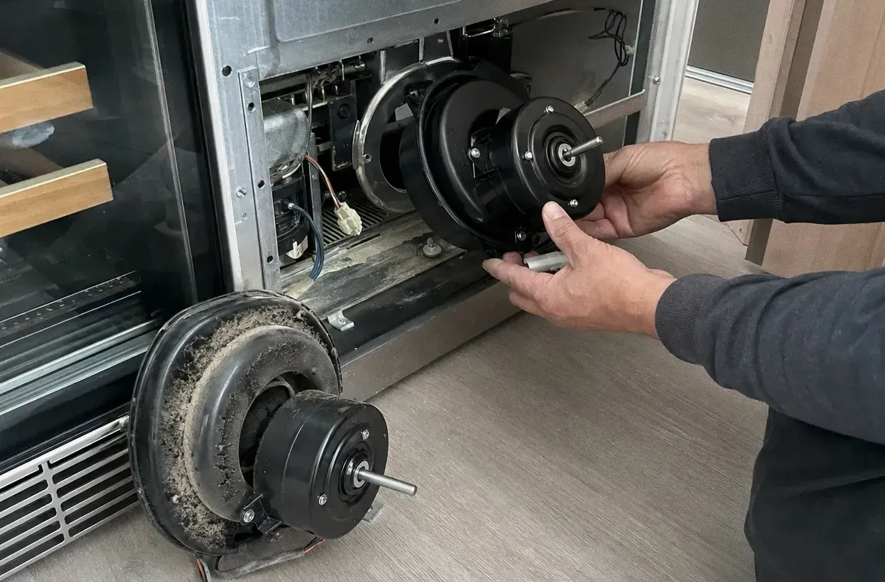 Rear panel removed from an appliance with a large blower motor being drawn out and a dust-caked squirrel-cage fan on the floor